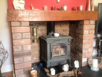 Brick fireplace with an oak beam mantel and a cast iron wood burner